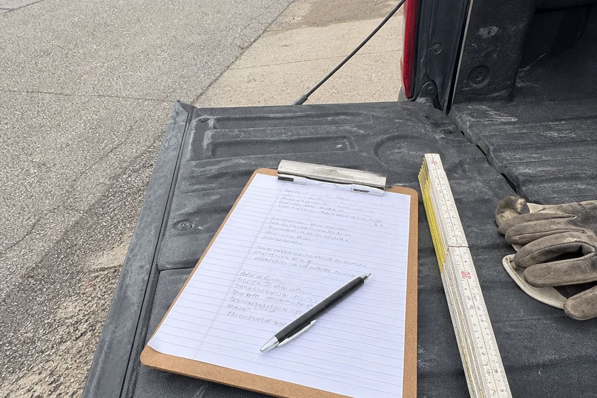 A clipboard with handwritten job notes and a pen resting on the open tailgate of a pickup truck.
