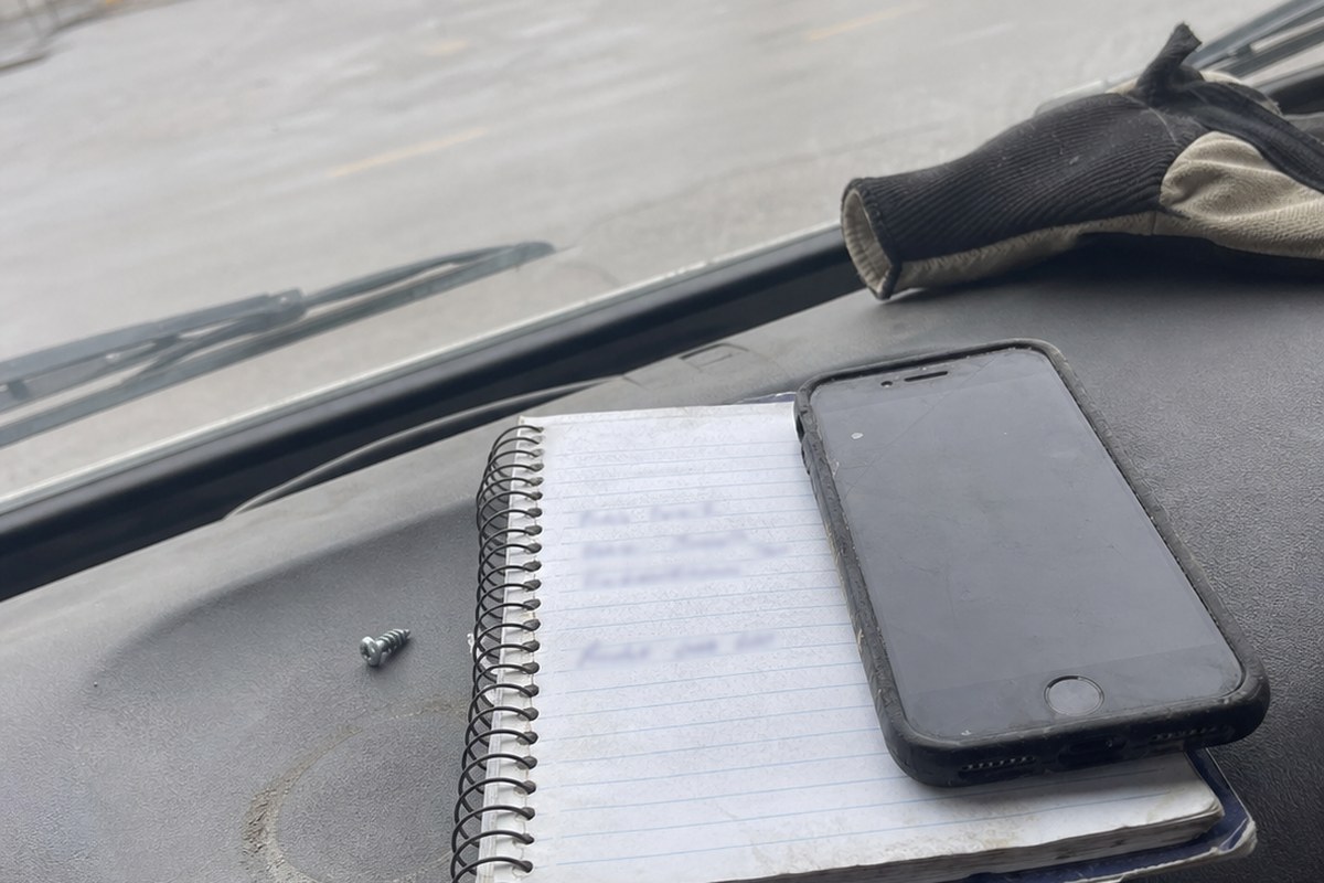 A small spiral notebook with handwritten call-back names and dates open on a truck dashboard next to a phone.